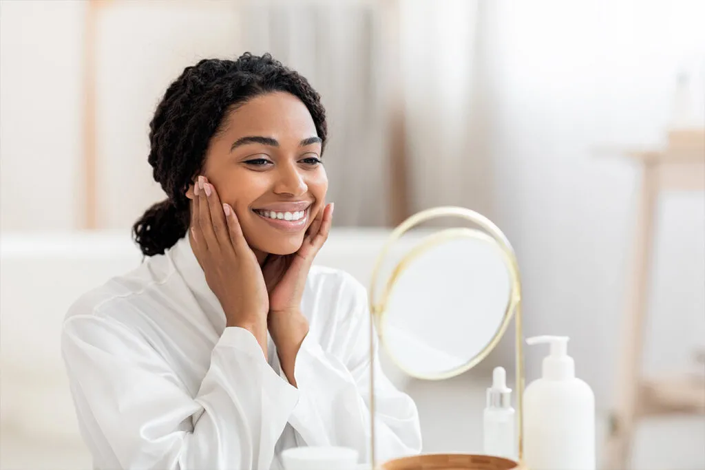 Woman smiling holding face in front of mirror